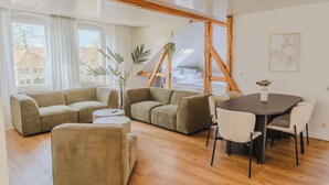 A modern living room with a sectional sofa, a round dining table with chairs, and a wooden ceiling. - Penthouse in Hildesheims Philosophen Viertel (Hildesheim)