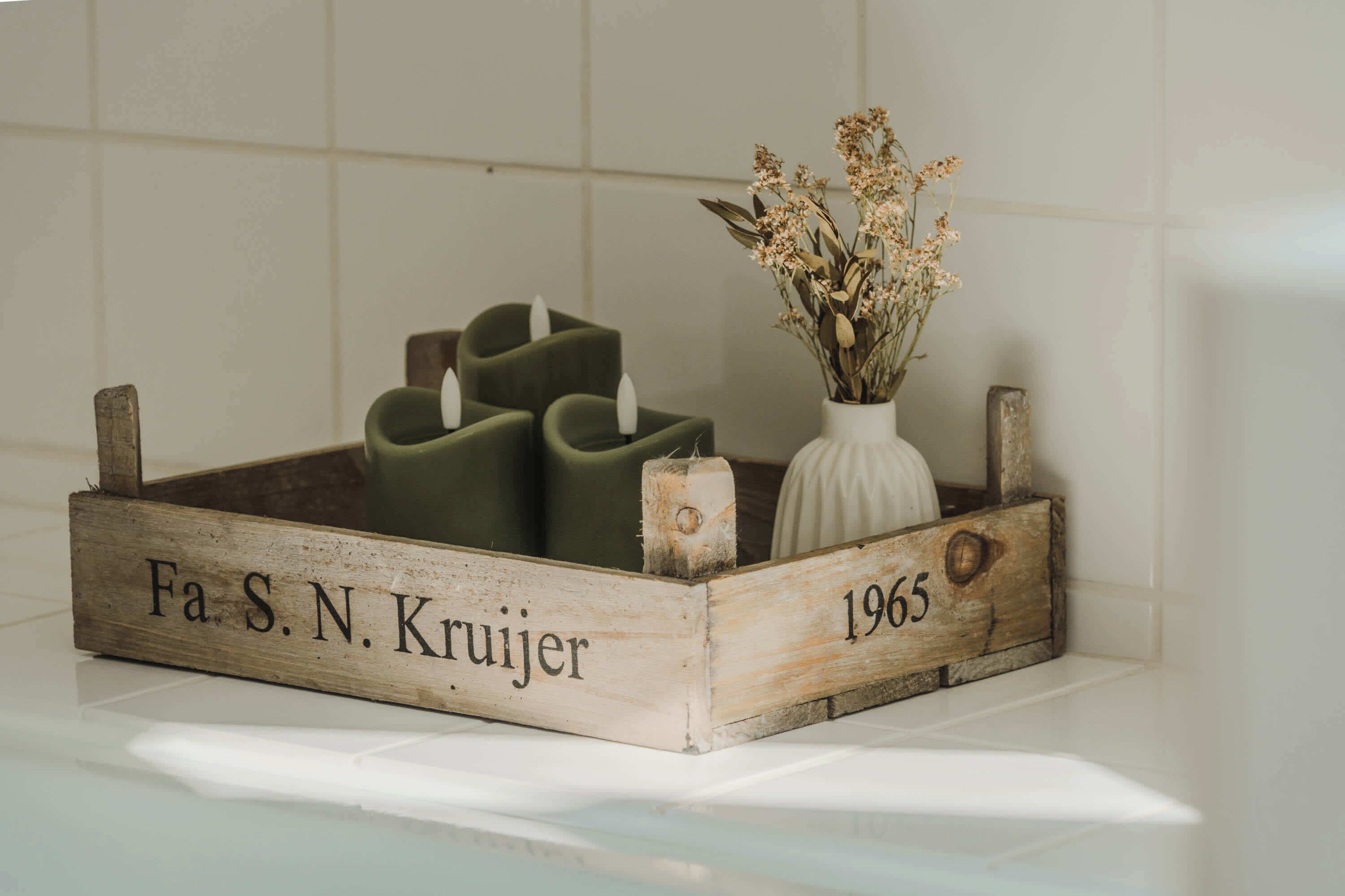 Una caja de madera con velas y flores secas, etiquetada "Fa S. N. Kruijer 1965".