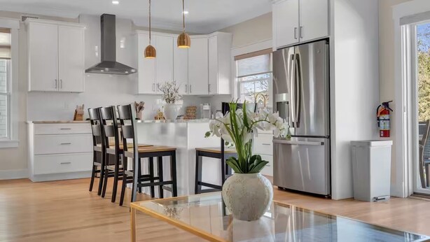 Una cocina moderna con armarios blancos, electrodomésticos de acero inoxidable y una mesa de comedor de vidrio.