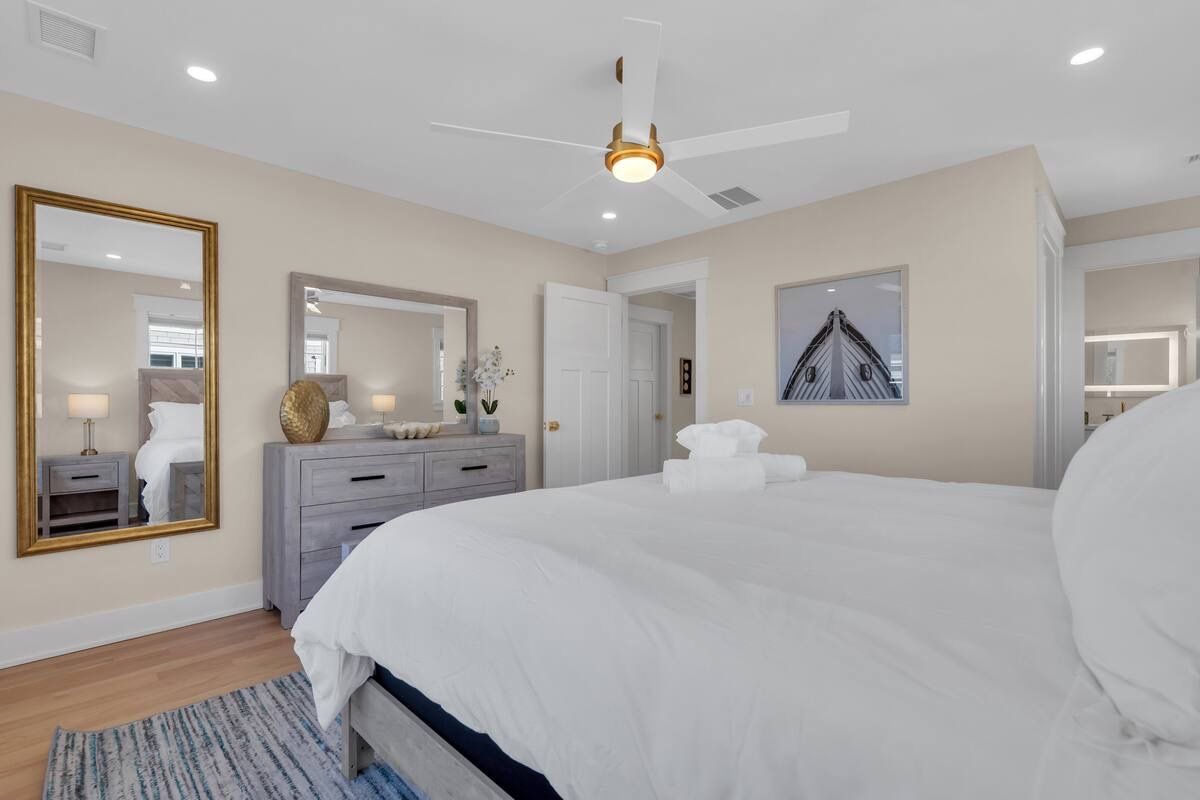 Un dormitorio con una cama grande, ventilador de techo, cómoda y espejo.