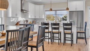 Una cocina moderna con armarios blancos, un refrigerador de acero inoxidable y un comedor con sillas y una mesa de madera.