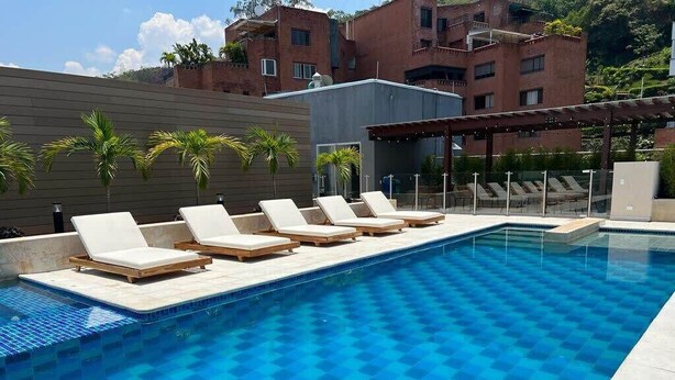 A swimming pool with lounge chairs, a pergola, and a view of buildings in the background. - H106 - Amazing Comfort & Amenities, Pool, Security (Cali)
