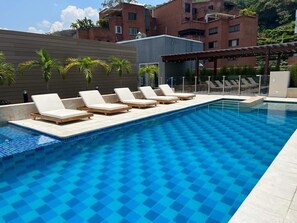 A swimming pool with checkered blue tiles, surrounded by lounge chairs and a pergola. - H107 - Perfect Holiday Pad | Pool | Parking | WiFi (Cali)