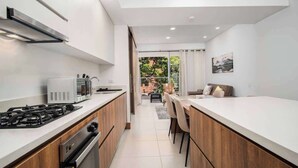 A modern kitchen with a gas stove, microwave, and oven. There is a dining area with a table and chairs. - H108 | 2-Bed, 2-Bath  | Pool | Gym | 24/7 Security (Cali)