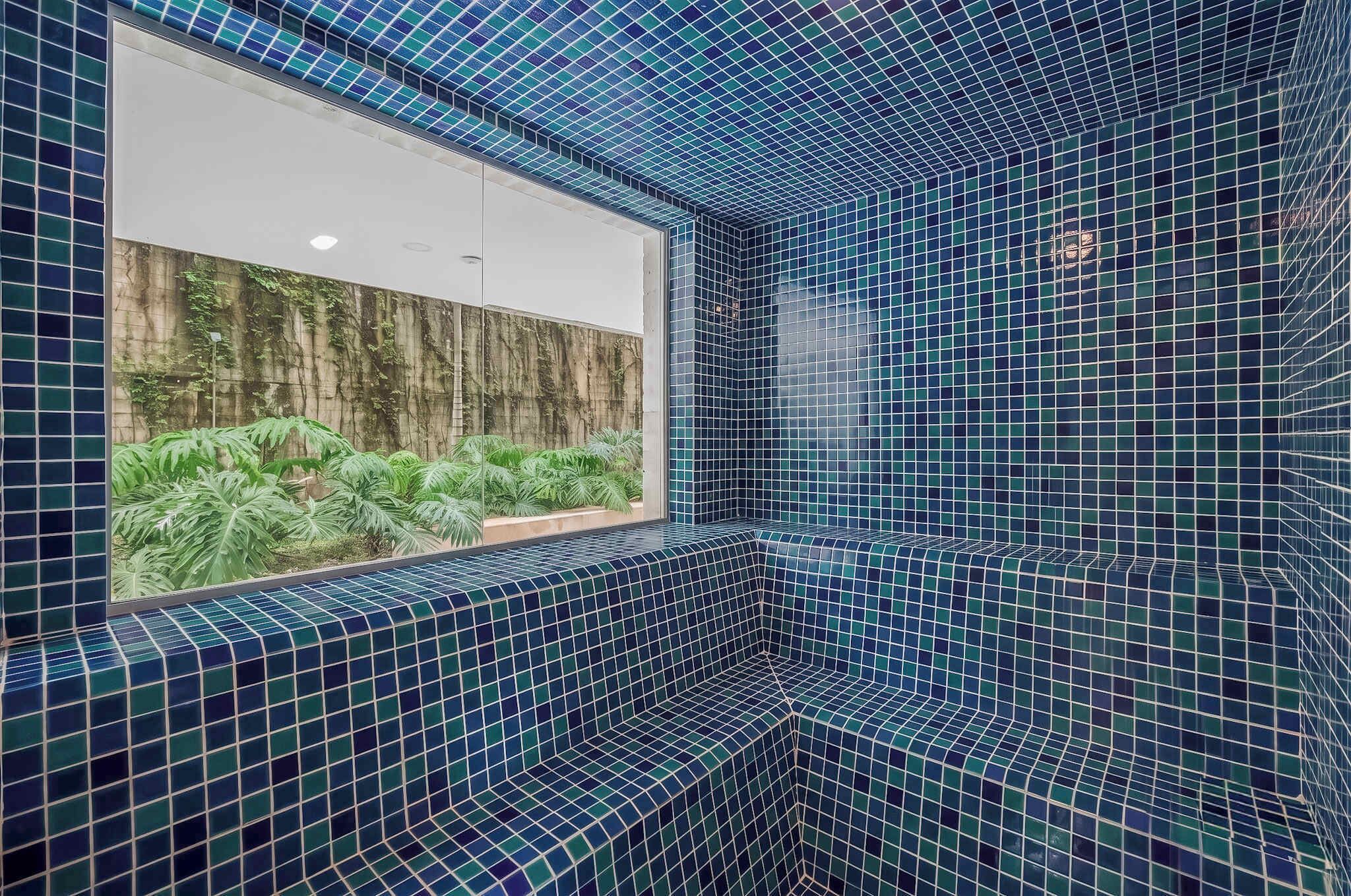 A corner of a room with blue-tiled walls and a window with a view of greenery.