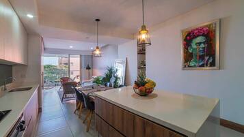 A modern kitchen with a central island, pendant lighting, and a dining area with chairs and a table.