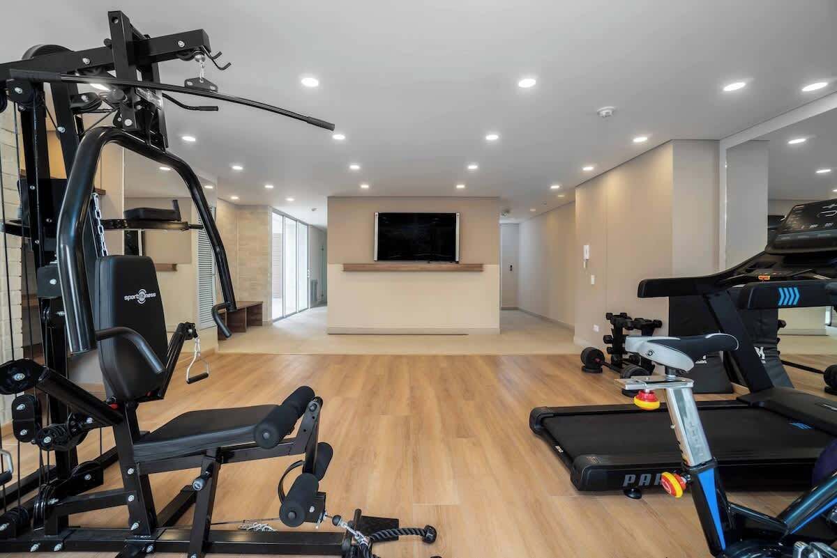 Une salle de sport à domicile équipée de matériel d’exercice, d’un tapis de course et d’un téléviseur fixé au mur.
