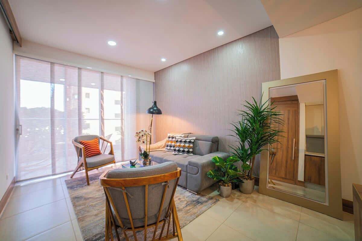 Een moderne woonkamer met een bank, fauteuil en een eettafel. Een groot raam zorgt voor natuurlijk licht en uitzicht.