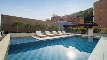 A swimming pool with lounge chairs, a pergola, and palm trees.