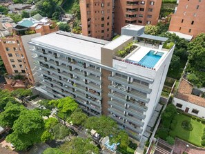 Um edifício alto com várias varandas, piscina no terraço e áreas verdes ao redor.