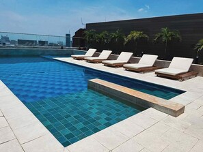 Une piscine sur le toit, avec des chaises longues et des palmiers.