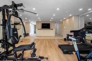 Une salle de sport à domicile équipée de matériel d’exercice, d’un tapis de course et d’un téléviseur fixé au mur.