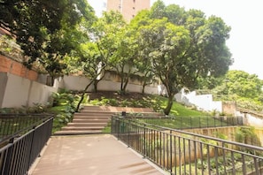 A pathway leading up a hill with metal railings, surrounded by lush greenery and trees.