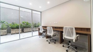 Un espacio de oficina moderno con dos sillas blancas, un escritorio de madera y un amplio ventanal que ofrece vistas a plantas al aire libre.