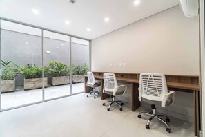 Een moderne kantoorruimte met twee witte bureaustoelen, een houten bureau en een grote glazen wand met uitzicht op buitenplanten.