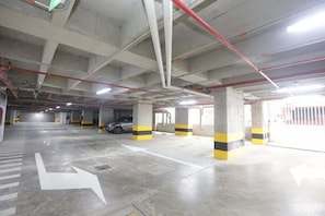 Un parking à plusieurs niveaux, avec des piliers en béton, des flèches directionnelles peintes sur le sol, et une voiture garée au loin.