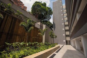 Een modern gebouw met een binnentuin, met een houten muur, een metalen hekwerk en diverse planten.