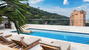 A swimming pool with lounge chairs, a clear sky, and a hill with buildings in the background. - H401 | top-Rated Cali Retreat 2BR w/ Balcony & Pool 24/7 Security + Free Parking (Cali)