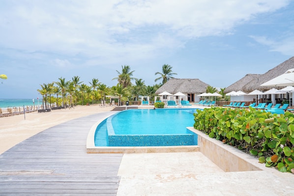 A pool area with a wooden deck, lounge chairs, and thatched-roof umbrellas.