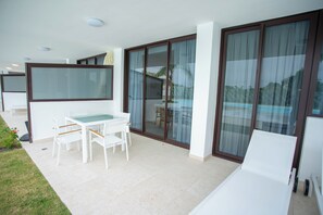 Een modern terras buiten met een eettafel en stoelen, grote schuifdeuren en een zwembad.