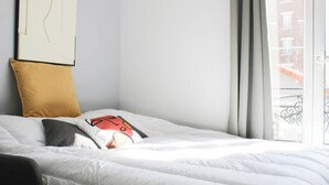 A neatly made bed with white bedding and a single pillow with a graphic design. - Charming T1 at the gates of Paris (Asnières-sur-Seine)