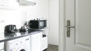 A compact kitchen with a washing machine, a microwave, and a kettle on the countertop. - Charming T1 at the gates of Paris (Asnières-sur-Seine)