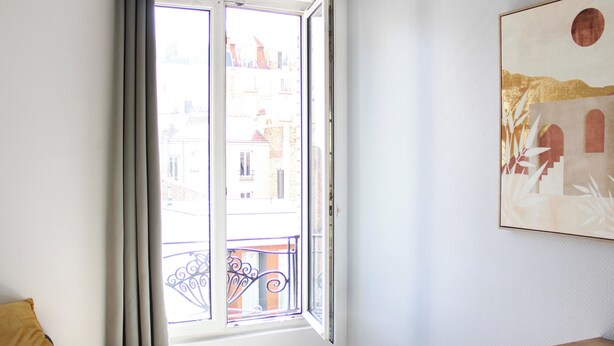 A room with a large window, a round table, and a piece of wall art. - Charming T1 at the gates of Paris (Asnières-sur-Seine)