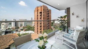 A balcony with a view of a cityscape, a white wicker sofa, and a potted plant. - H604 - Beautiful View with Balcony, Pool & Parking (Cali)