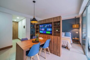 Um espaço de estar moderno com uma mesa de jantar de madeira, cadeiras azuis, uma televisão de tela plana e uma cama com cabeceira azul.