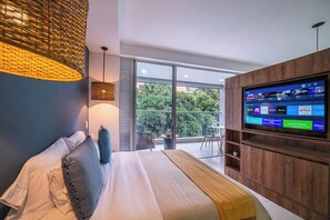 Quarto moderno com cama grande, televisão na parede e varanda com vista para vegetação.
