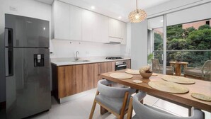 A modern kitchen with a stainless steel refrigerator, wooden cabinets, and a dining area with a table and chairs. - H702 - Amazing Balcony | Pool | Gym | Near Granada (Cali)