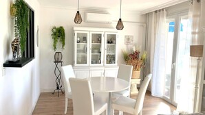 A dining area with a white table and chairs, a white cabinet with glass doors, and hanging plants.