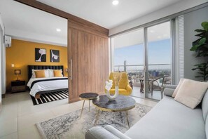Una moderna camera d'hotel con un letto, un divano, un'area pranzo e un balcone con vista sulla città.