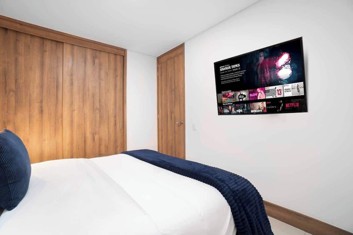 Une chambre à coucher avec un lit, une armoire en bois et un téléviseur fixé au mur qui affiche une affiche de film.