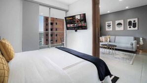A modern hotel room with a large bed, a TV mounted on the wall, a balcony with a view of a brick building, and a sofa in the living area. - H706 - Stylish 2BR / Perfect Views & Rooftop Pool (Cali)