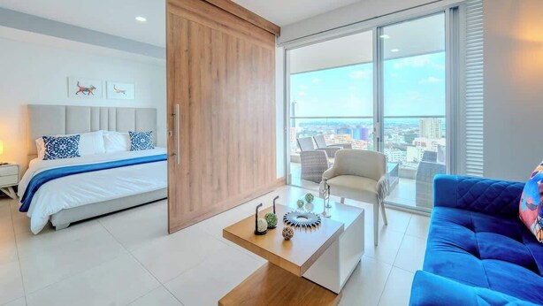 A modern hotel room with a bed, a coffee table, a sofa, and a large window offering a city view. - H807 - Amazing Penthouse Views, Pool and Parking (Cali)