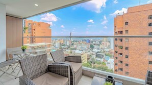 A balcony with wicker furniture, a glass table, and a view of a cityscape. - H807 - Amazing Penthouse Views, Pool and Parking (Cali)