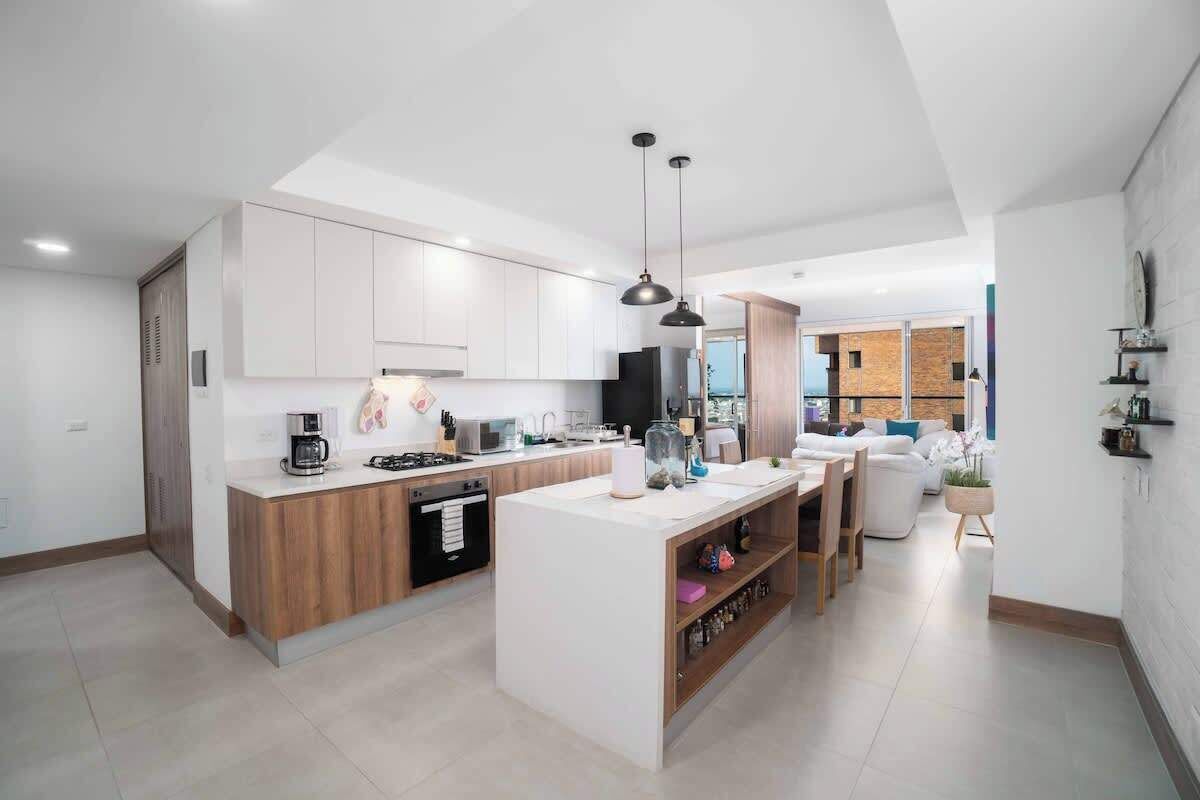 Een moderne keuken met witte kasten, een centraal eiland en hangende lampen.