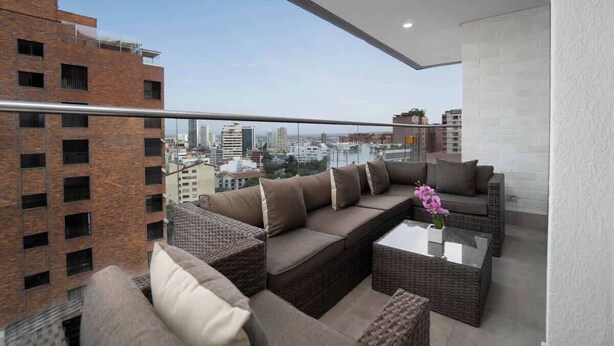 Un balcón con un sofá, una mesa de centro y un jarrón de flores.