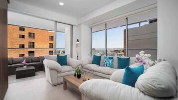 Un salon moderne avec un grand ensemble de canapés, une table basse et une vue sur un bâtiment en briques, visible à travers de grandes fenêtres.