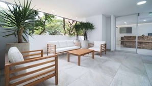 Un espacio interior moderno con un sofá y dos sillas de madera, una mesa de centro y plantas en macetas.