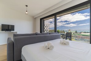 A modern hotel room with a large bed, grey sofa, and a TV mounted on the wall. - Fenix III (Funchal)