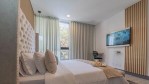 Una habitación de hotel moderna con una cama grande, un televisor de pantalla plana montado en la pared y vistas al exterior por la ventana.