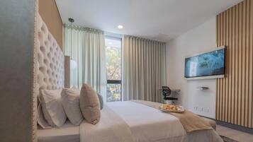 A modern hotel room with a large bed, a flat-screen TV mounted on the wall, and a view of the outdoors through the window.