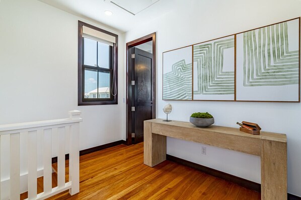 Un couloir doté d’un plancher en bois, d’une rambarde blanche, d’une porte et d’une console sur laquelle sont posés une plante et des objets décoratifs.