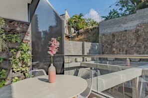 Ein moderner Essbereich im Freien mit Glasgeländer, einem weißen Tisch und einer rosa Vase.