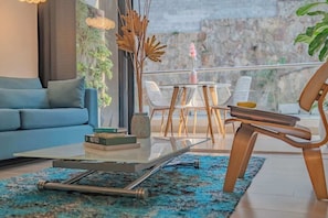 A modern living room with a sofa, a glass coffee table, and a view of a balcony with chairs. - RM 308 | Luxury | Pool & Parking | Santa Teresita (Cali)