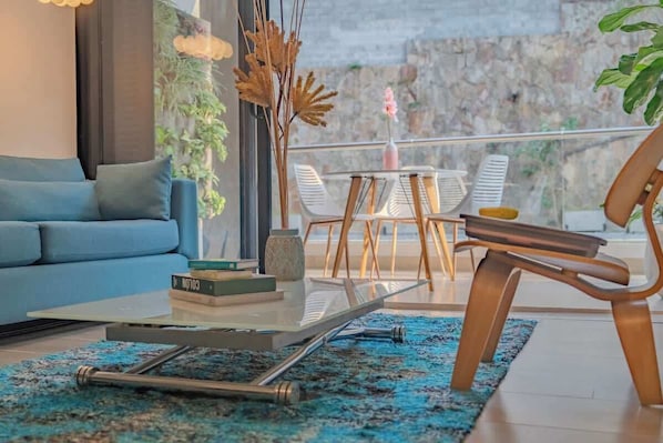 A modern living room with a sofa, a glass coffee table, and a view of a balcony with chairs. - RM 308 | Luxury | Pool & Parking | Santa Teresita (Cali)
