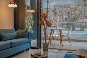 Ein modernes Wohnzimmer mit einer Couch, einem Glastisch, einer Vase mit Trockenblumen und einem Essbereich mit Tisch und Stühlen.