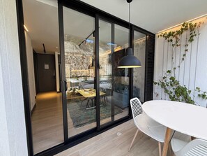 Ein modernes Interieur mit einer Schiebeglas-Tür, die in einen Essbereich führt, einem weißen Tisch und einer hängenden Pendelleuchte.